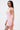 A person with long straight hair models the ALL EYES ON ME MINI DRESS IN PINK, featuring a ruched design and deep side cutouts, standing sideways against a plain white background.