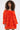 A woman with curly hair models the IN THE NAME OF FASHION RUFFLE MINI DRESS, an off-the-shoulder, bright orange mini dress with ruffled, fluffy fabric and long sleeves, posing against a plain light background.