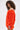 A woman with curly hair showcases the IN THE NAME OF FASHION RUFFLE MINI DRESS, a bright orange, off-the-shoulder mini with textured fabric and ruffled details, set against a plain white background.