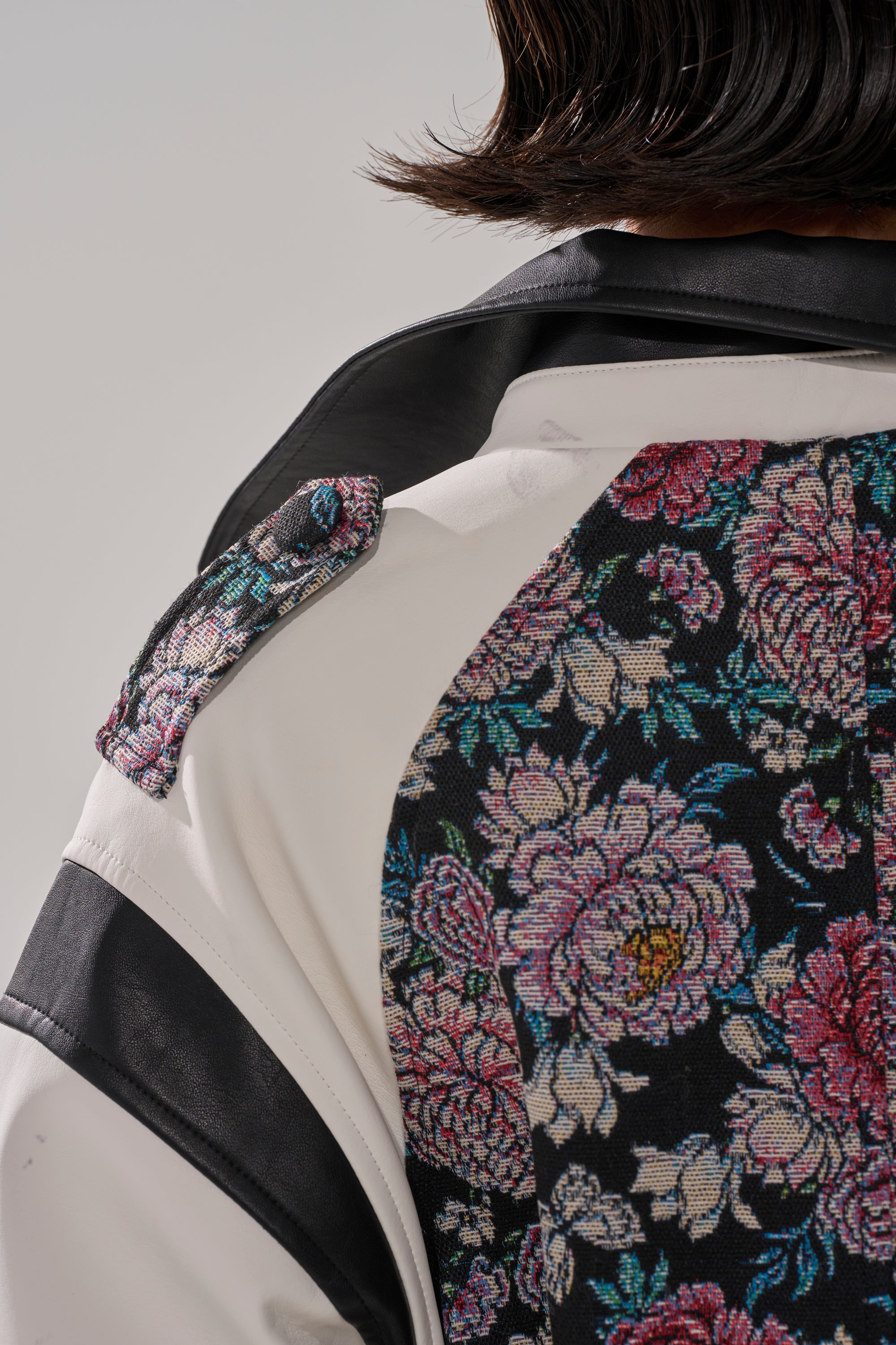 Close-up of the END GAME MIXED MEDIA TRENCH, showing the back and shoulder with a black floral panel featuring pink and white flowers, white sections, and black trim.