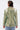 A person with short, slicked-back hair is shown from behind wearing the DON'T TRY ME EMBELLISHED BROCADE BLAZER, a green statement piece with white and black striped accents, and holding a circular gold accessory in their left hand.