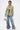 A person stands confidently in the DON'T TRY ME EMBELLISHED BROCADE BLAZER over a lace bralette, oversized ruched denim pants, heeled sandals, layered jewelry, and holds a spherical gold handbag against a plain white background.