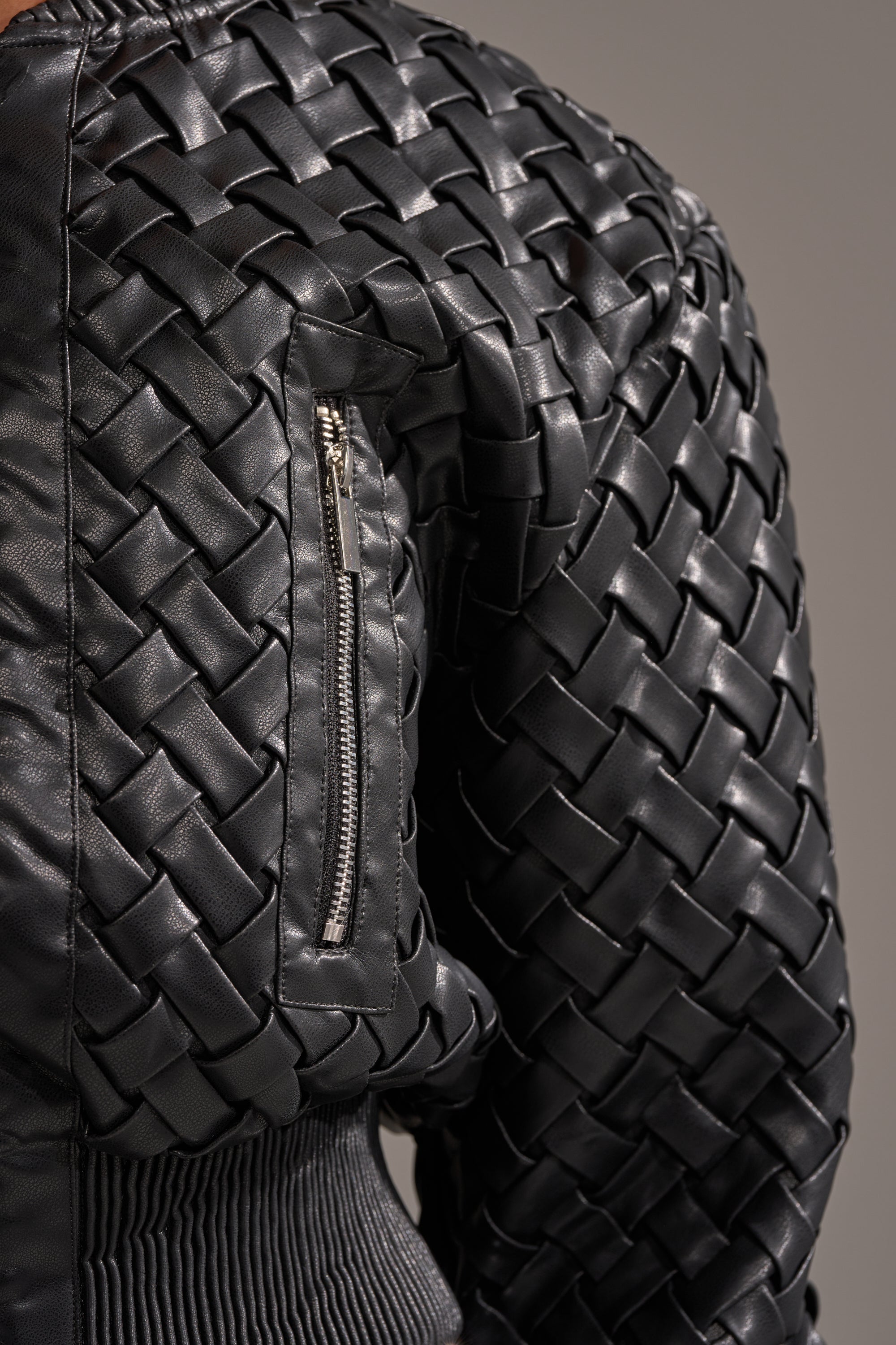 Close-up of the WICKER PARK WOVEN BOMBER in black, showing its wicker weave, ribbed cuff detail, and a small zippered sleeve pocket.