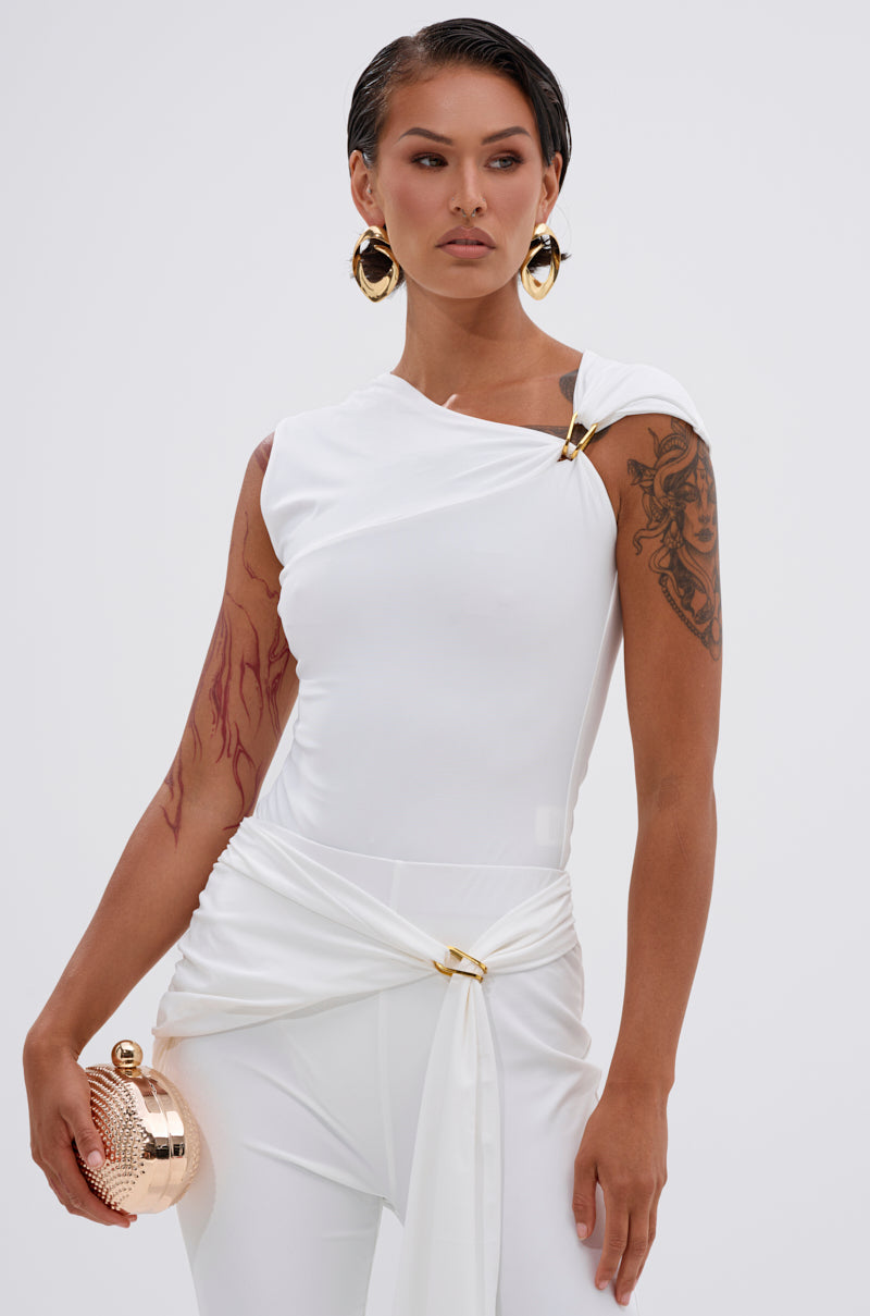 A woman with short dark hair and visible arm tattoos wears the white IZZY SEAMLESS BODYSUIT, styled with gold accents, large hoop earrings, and a round gold clutch, standing against a plain light background. 0
