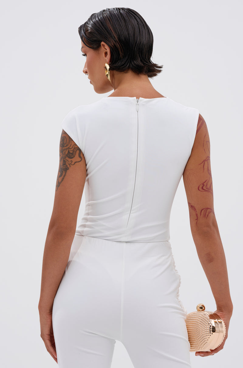 A person wearing the IZZY SEAMLESS BODYSUIT stands with their back to the camera, revealing a back zipper. They have short dark hair, gold hoop earrings, arm tattoos, and hold a small round beige clutch in their right hand. 4