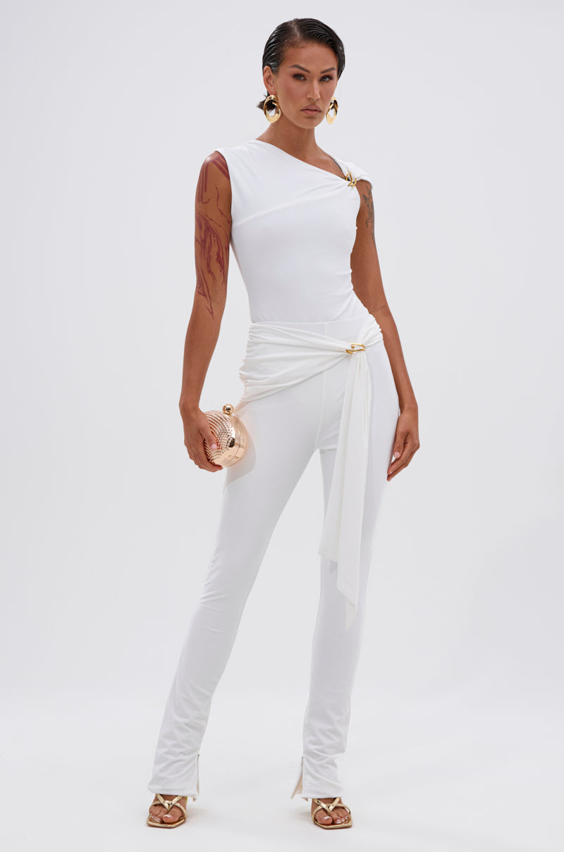 A woman exudes confidence in the IZZY SEAMLESS BODYSUIT, a fitted all-white piece with single-shoulder detail and sash. She styles it with a gold clutch, gold hoop earrings, strappy heels, and shows off arm tattoos. 6
