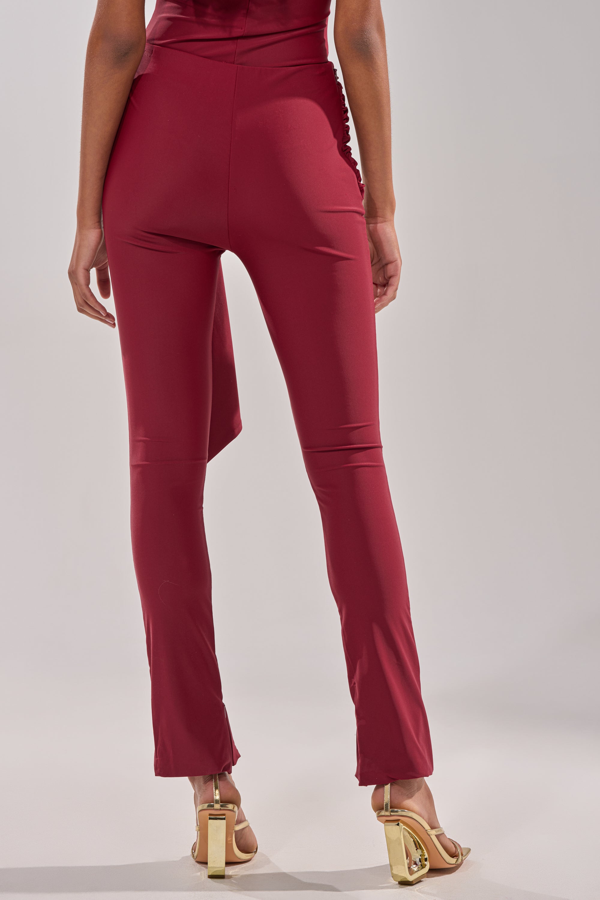A person shown from the back, waist down, wearing the IZZY SEAMLESS LEGGING IN BURGUNDY with gold high-heeled sandals, set against a plain light background. 5