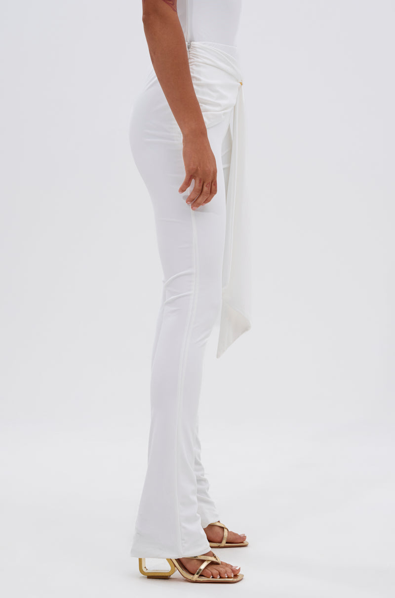 A person stands sideways wearing the fitted IZZY SEAMLESS LEGGING in white, paired with a matching wrap detail top and white square-toe heeled sandals. The background is plain white. 2