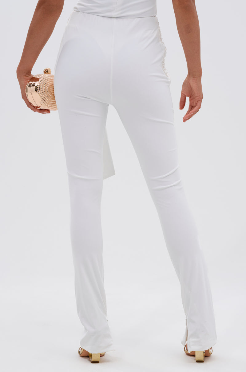 A person stands facing away, wearing the fitted IZZY SEAMLESS LEGGING in white, made from body-contouring fabric, and holding a small shiny gold clutch against a plain white background. 3