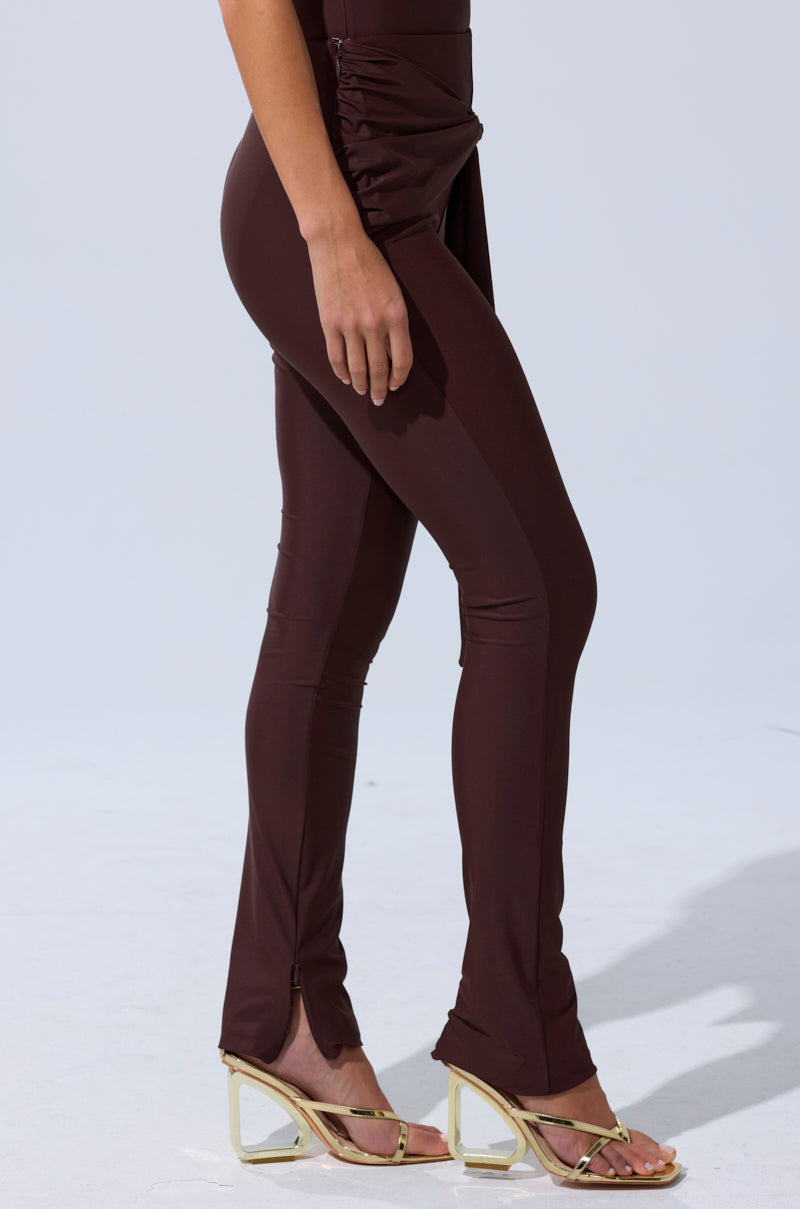 A person wearing KIMMY SEAMLESS LEGGING IN BROWN, featuring a fitted, body-contouring design with decorative ruching and gold heeled sandals, stands on a light gray surface. Only the lower half of the body is visible. 4