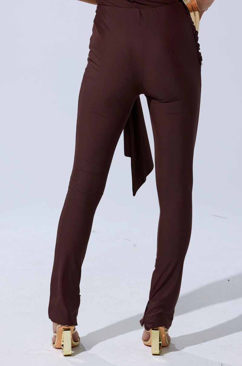 A person wearing KIMMY SEAMLESS LEGGING IN BROWN and gold-heeled sandals stands on a light-colored floor, viewed from the back. 5