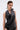 A woman with slicked-back hair wears the KRISTIN SATIN BLOUSE, a sleeveless black halter top featuring draped details, paired with black lace bottoms, standing against a plain light background.