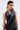 A woman with slicked-back hair wears the KRISTIN SATIN BLOUSE, a sleeveless draped black halter top, paired with black lace-trimmed bottoms, posing against a plain light gray background.