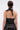 A person with wet, slicked-back hair is shown from behind wearing the KRISTIN SATIN BLOUSE in black with a strapless, tied halter neck style and lace-patterned black bottoms against a plain light gray background.