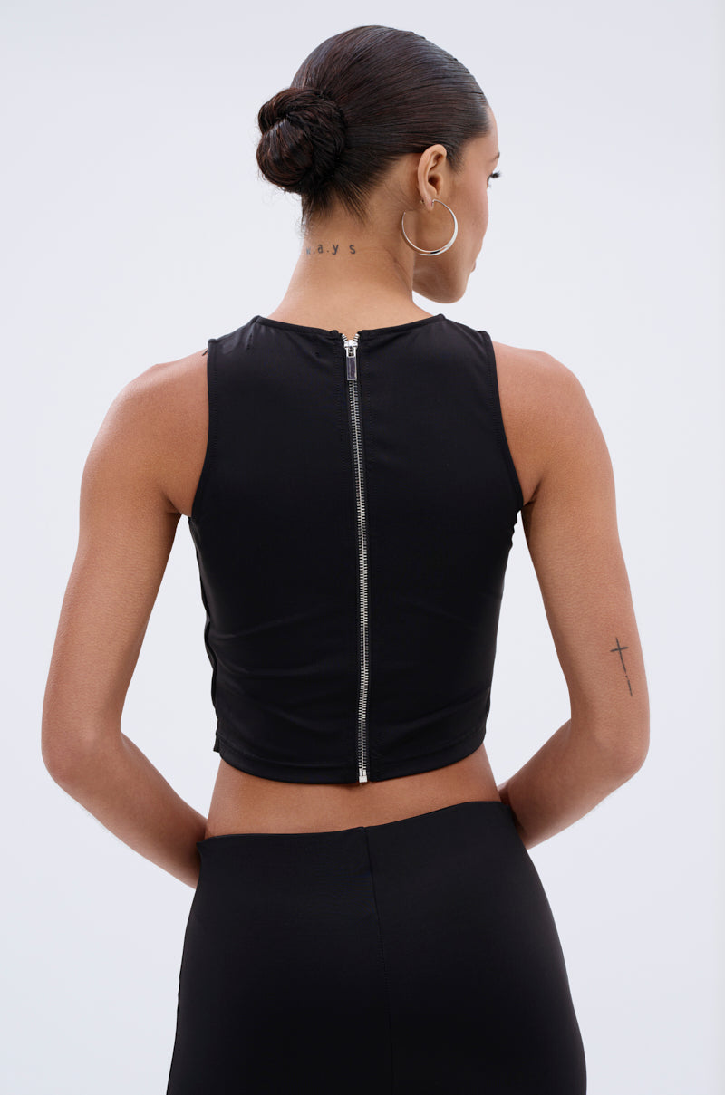 A woman with her hair in a low bun is shown from the back, wearing the GROMMET DETAIL RUCHED TANK TOP and a black skirt. She has a cross tattoo on her left arm and another tattoo on her neck. 3