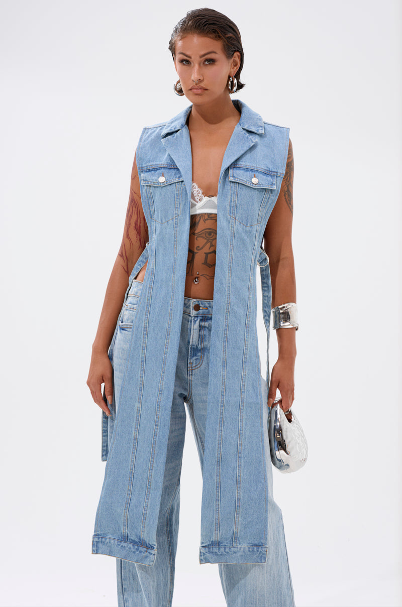 A person wears wide-leg jeans and the DOWN TO IT SPLIT DENIM VEST over a white lace bra, accessorized with a silver bracelet and small metallic handbag, standing against a plain white background. 0