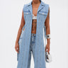 A person wears wide-leg jeans and the DOWN TO IT SPLIT DENIM VEST over a white lace bra, accessorized with a silver bracelet and small metallic handbag, standing against a plain white background.