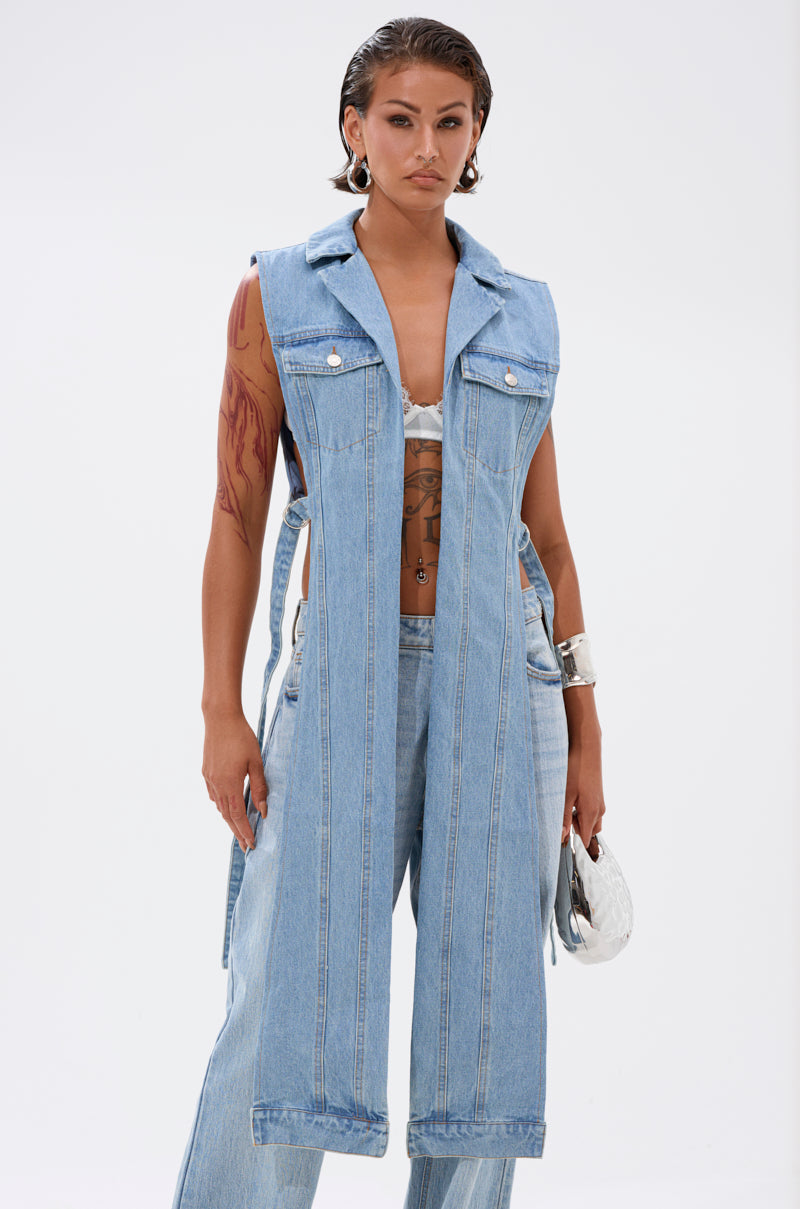 Wearing the DOWN TO IT SPLIT DENIM VEST over a white bralette and light-wash denim pants, paired with silver jewelry and a silver purse, this streetwear look stands out against a plain white background. 1