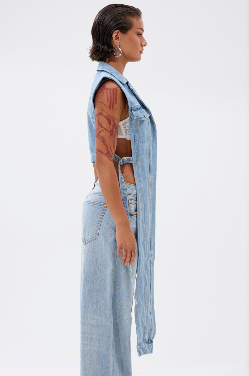 A woman in profile against a white background wears light blue jeans and the DOWN TO IT SPLIT DENIM VEST over a white top, styled with short wet-look hair and a visible large upper arm tattoo for a streetwear edge. 2