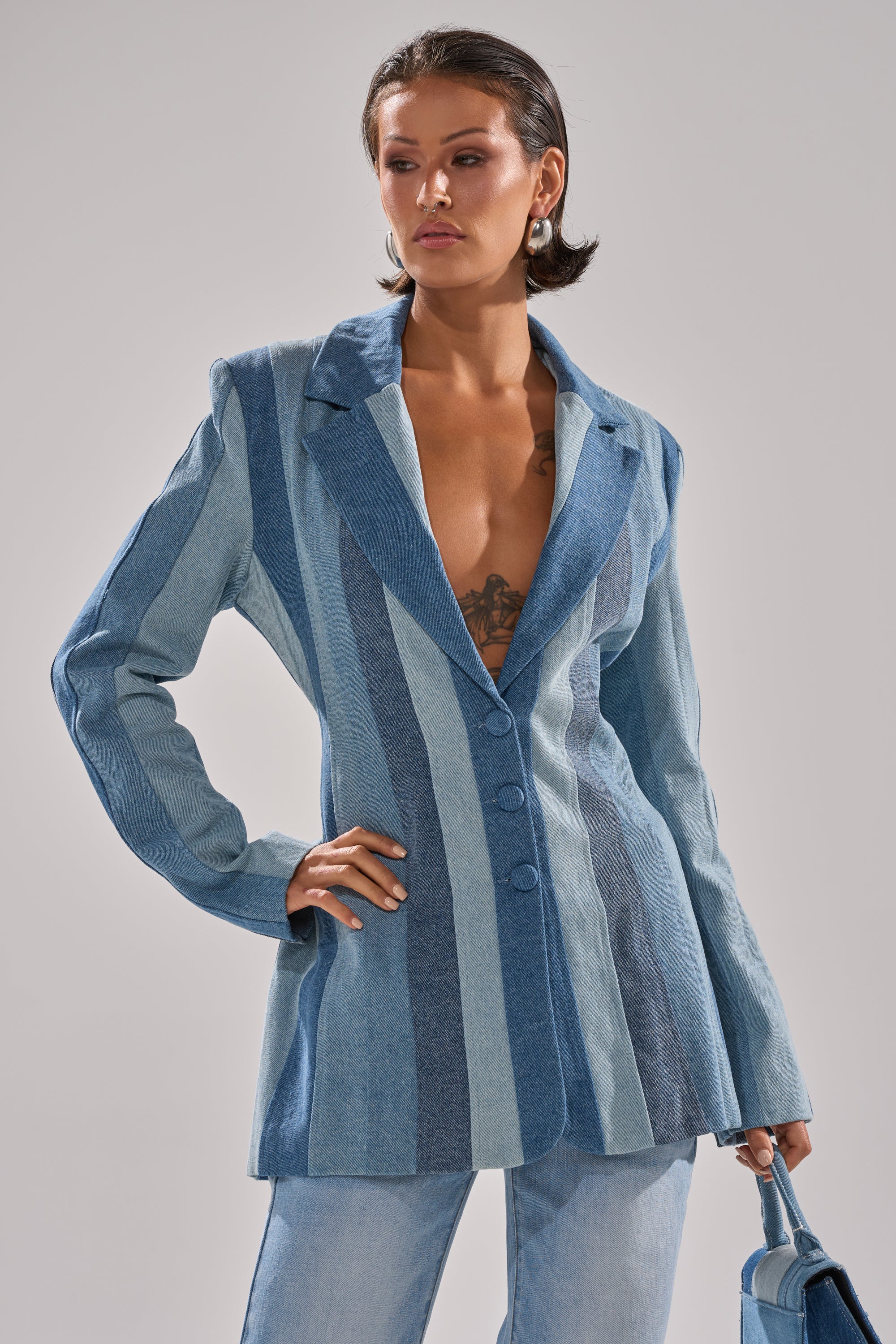 A woman with short brown hair models the COME SLIDE PATCHWORK DENIM BLAZER in blue shades, styled with light blue jeans and a small blue handbag, posing confidently against a plain background.