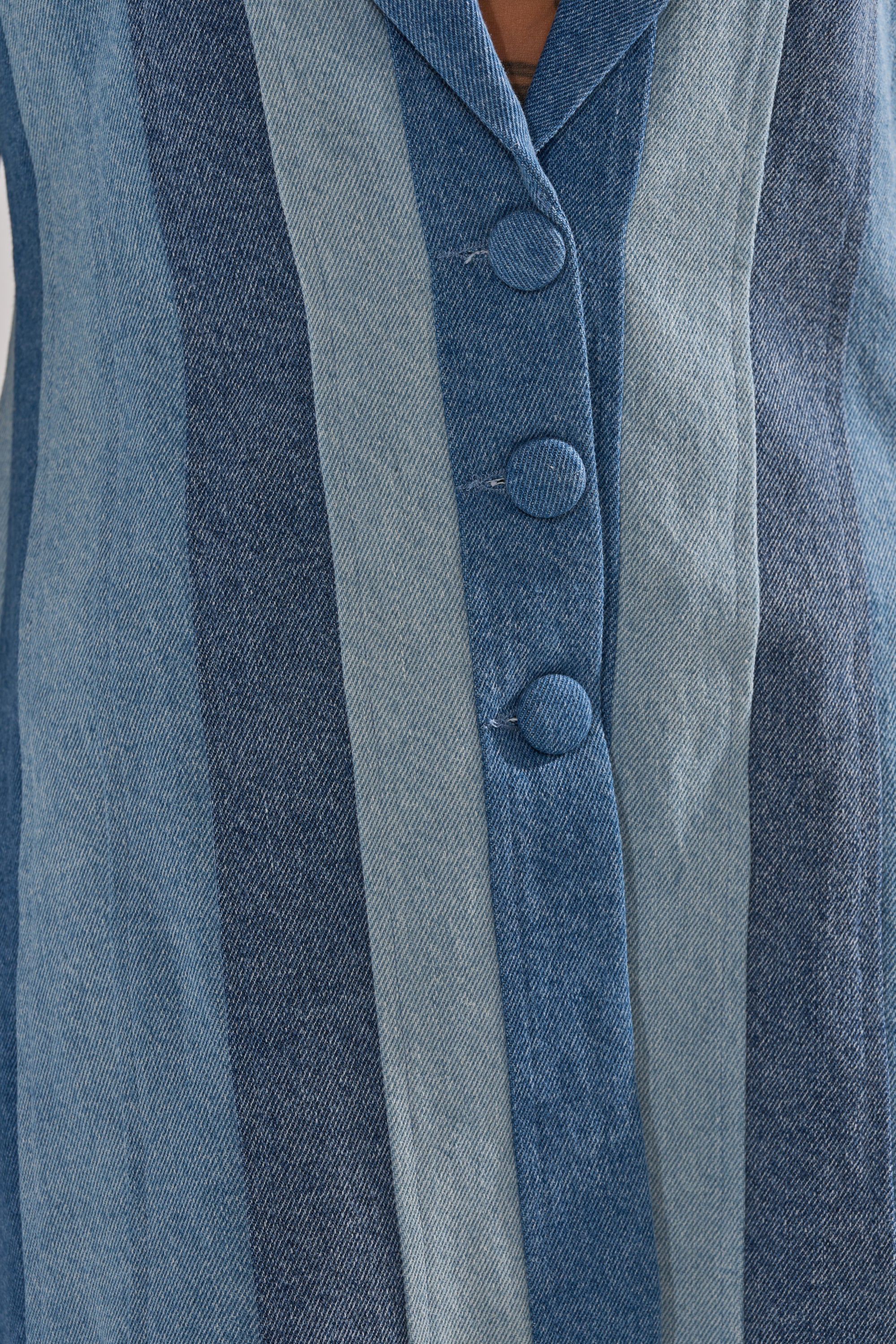 Close-up of the COME SLIDE PATCHWORK DENIM BLAZER, showcasing vertical blue stripes in different shades and large round buttons down the center.