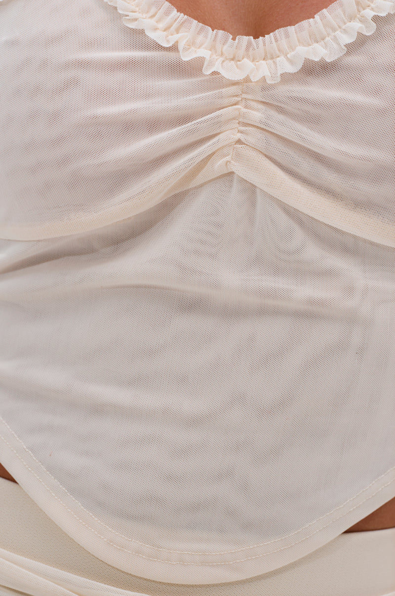 Close-up of a person wearing the MELISSA MESH CAMI, a sheer cream-colored cropped top with ruched bust, ruffled neckline trim, soft gathers at the center, and lightweight, slightly transparent mesh fabric for an airy feel. 6
