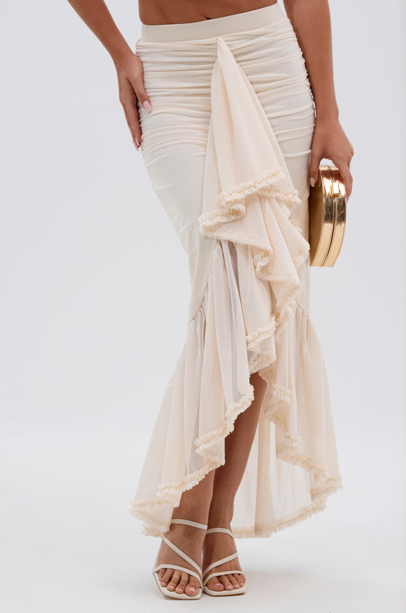 A woman wearing the MELISSA MESH RUCHED SKIRT in cream, holding a gold clutch and strappy white sandals. The photo is cropped from the waist down against a plain background. 0