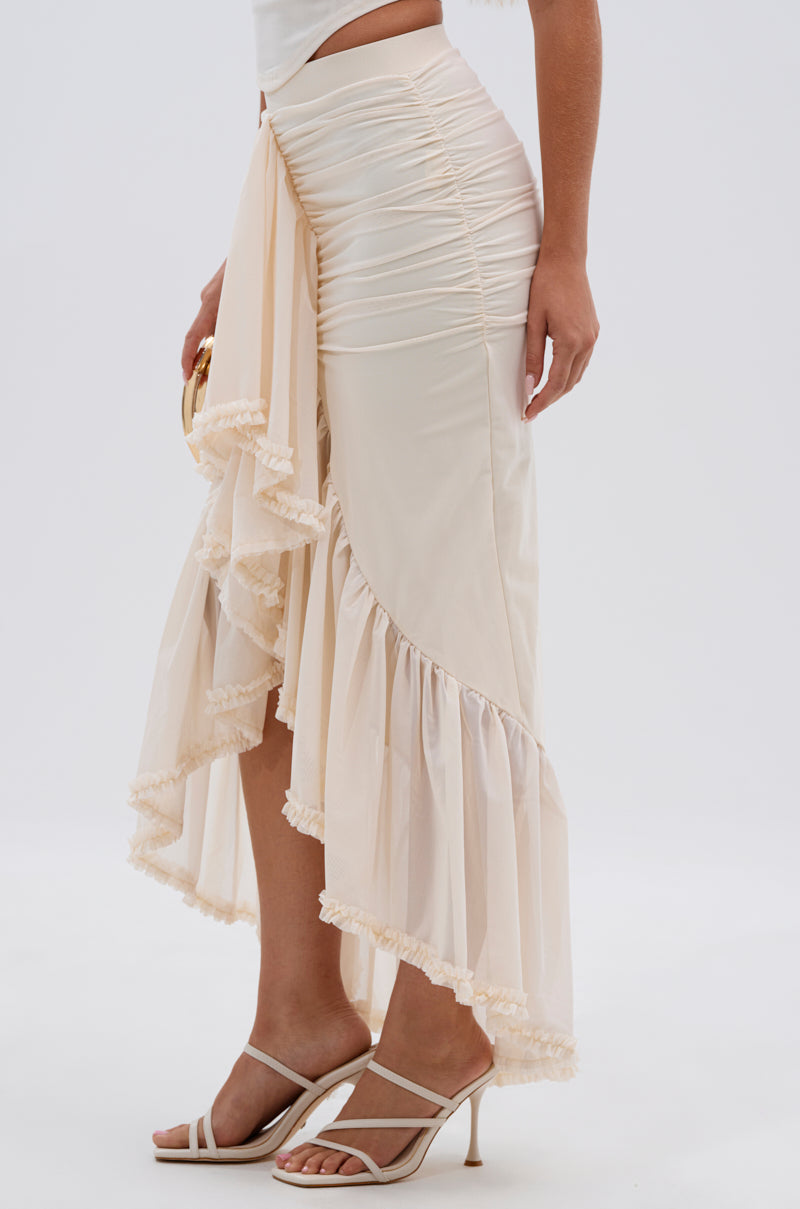 A person wearing the MELISSA MESH RUCHED SKIRT, featuring cream-colored mesh with ruching and sheer ruffles, paired with a white top and white heeled sandals, standing against a plain background. 2