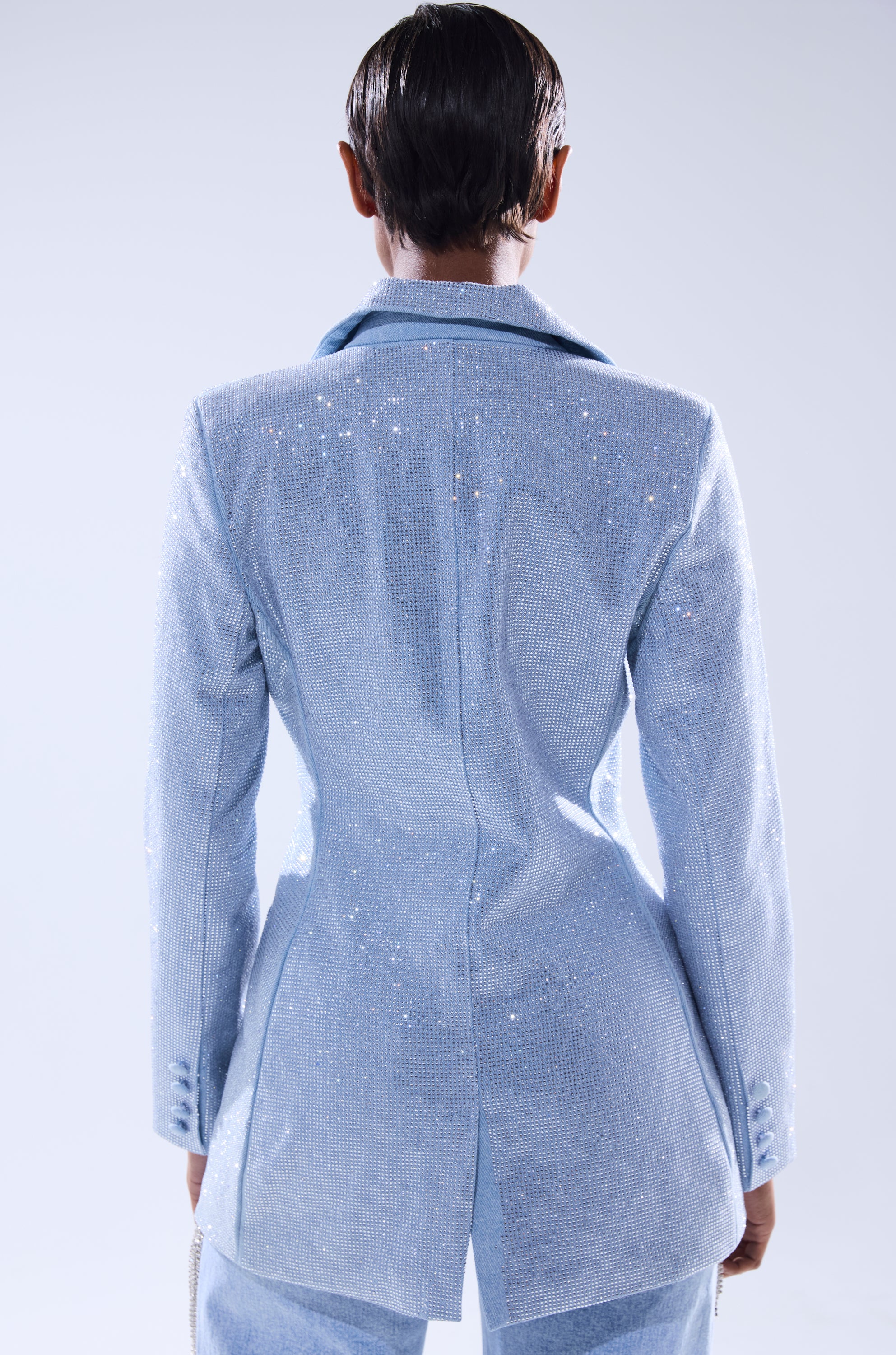 A person with short, slicked-back hair is seen from behind wearing the HERE FOR A GOOD TIME EMBELLISHED BLAZER, its shimmering rhinestones and light blue color standing out against a plain background. 4