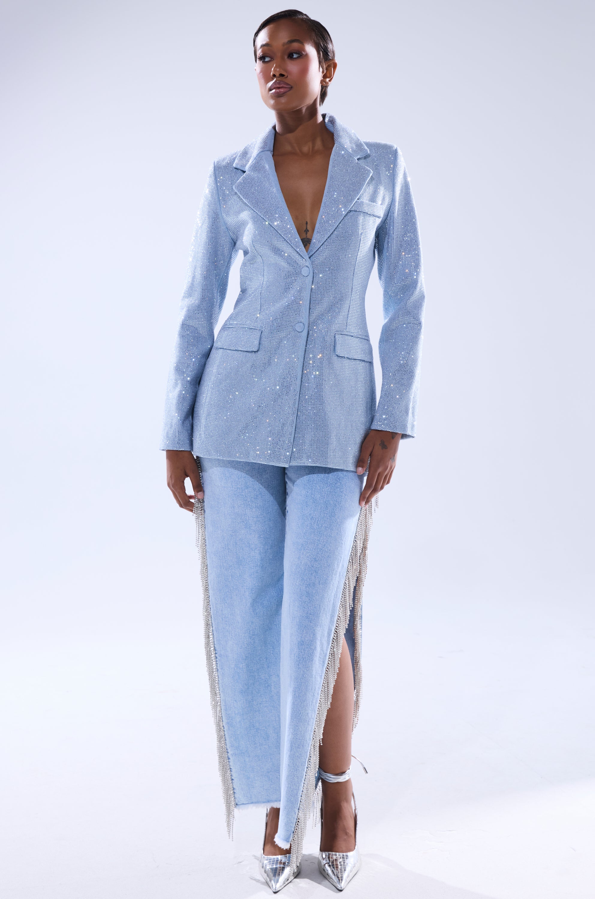 A woman poses confidently in the HERE FOR A GOOD TIME EMBELLISHED BLAZER, a pale blue jacket with rhinestone accents, paired with matching fringe wide-leg pants and shiny silver heels against a plain light background. 7