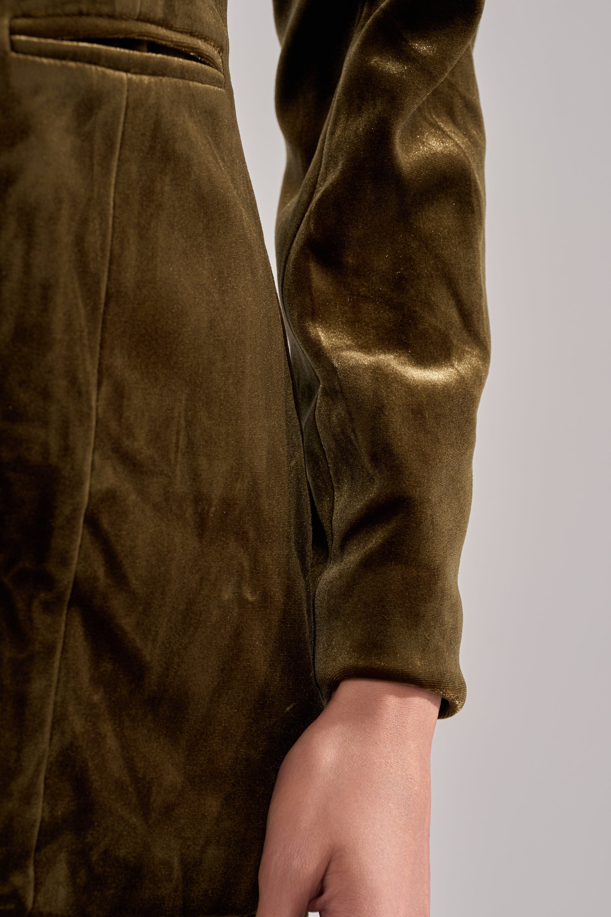 Close-up of a person wearing the DIRTY MARTINI VELVET BLAZER in brown, highlighting the sleeve, part of the torso, and hand against a plain light background.
