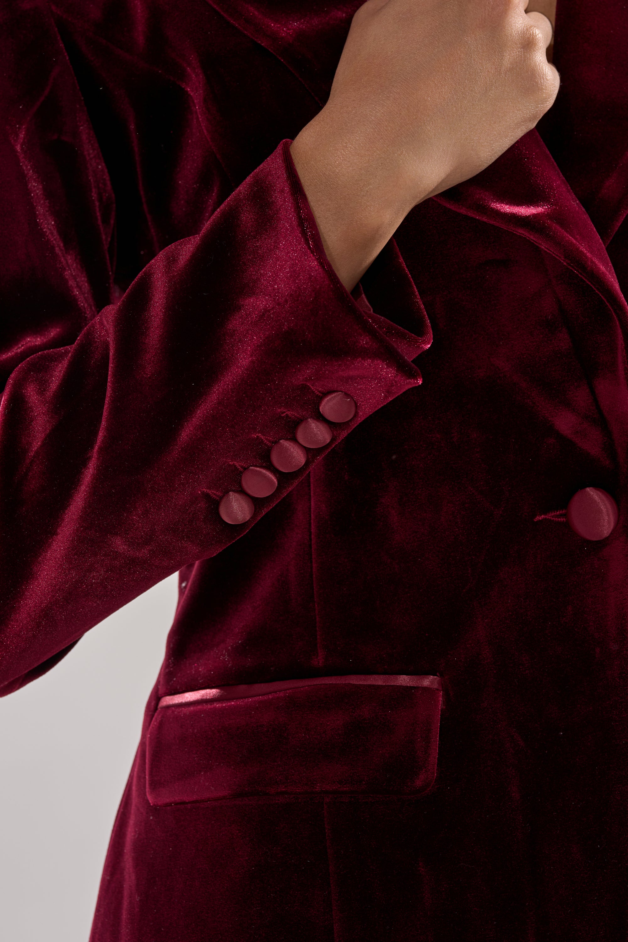 A person wearing the LUXE VELVET TUXEDO BLAZER holds the lapel, showcasing the rich texture, detailed sleeve, pocket, and buttoned cuff, highlighting the elegance of this classic tailored piece.