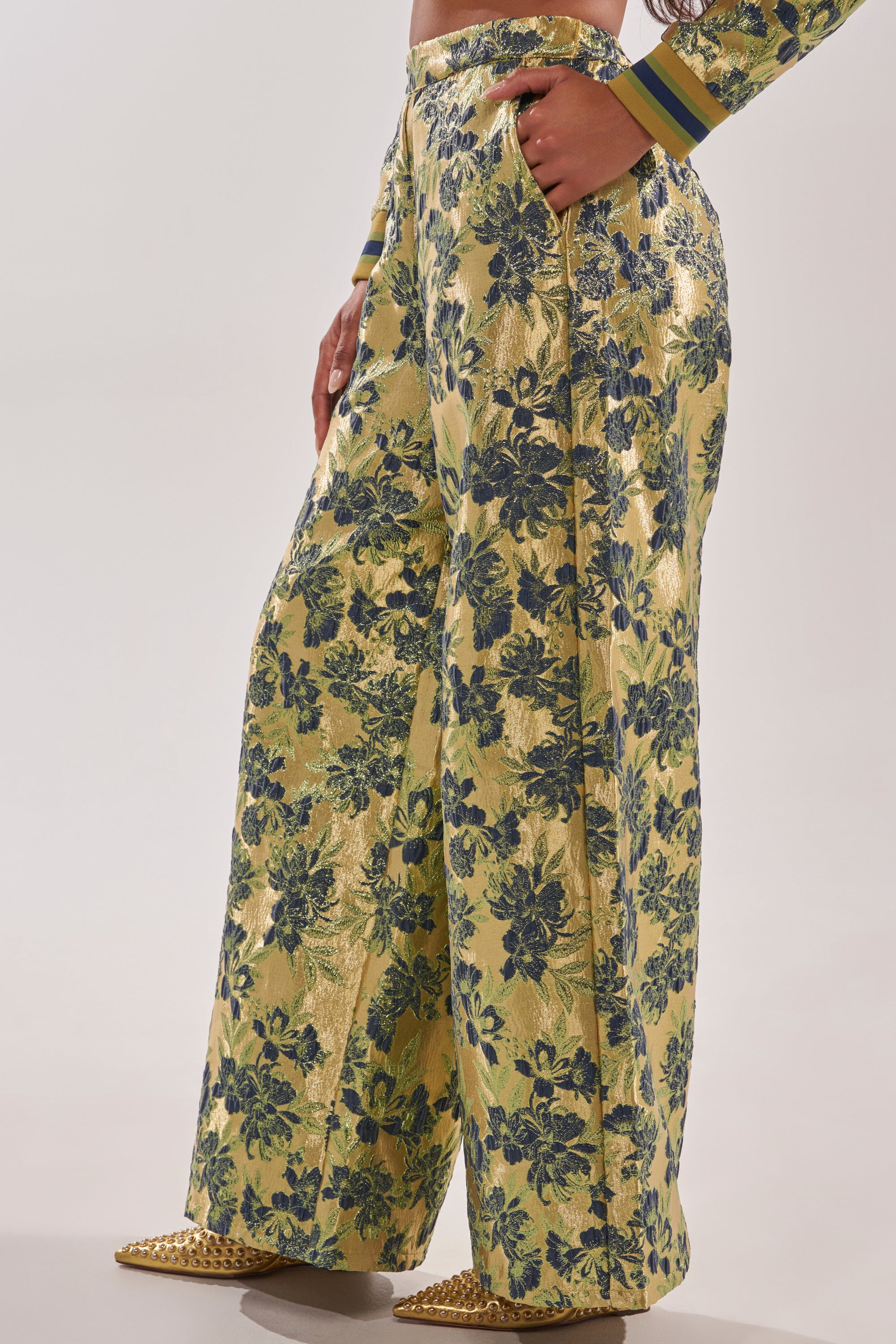 A person wearing HARLOW BROCADE WIDE LEG PANT—high-waisted trousers with a yellow and blue floral design—and pointed yellow shoes. The photo is cropped from the shoulders down. 3