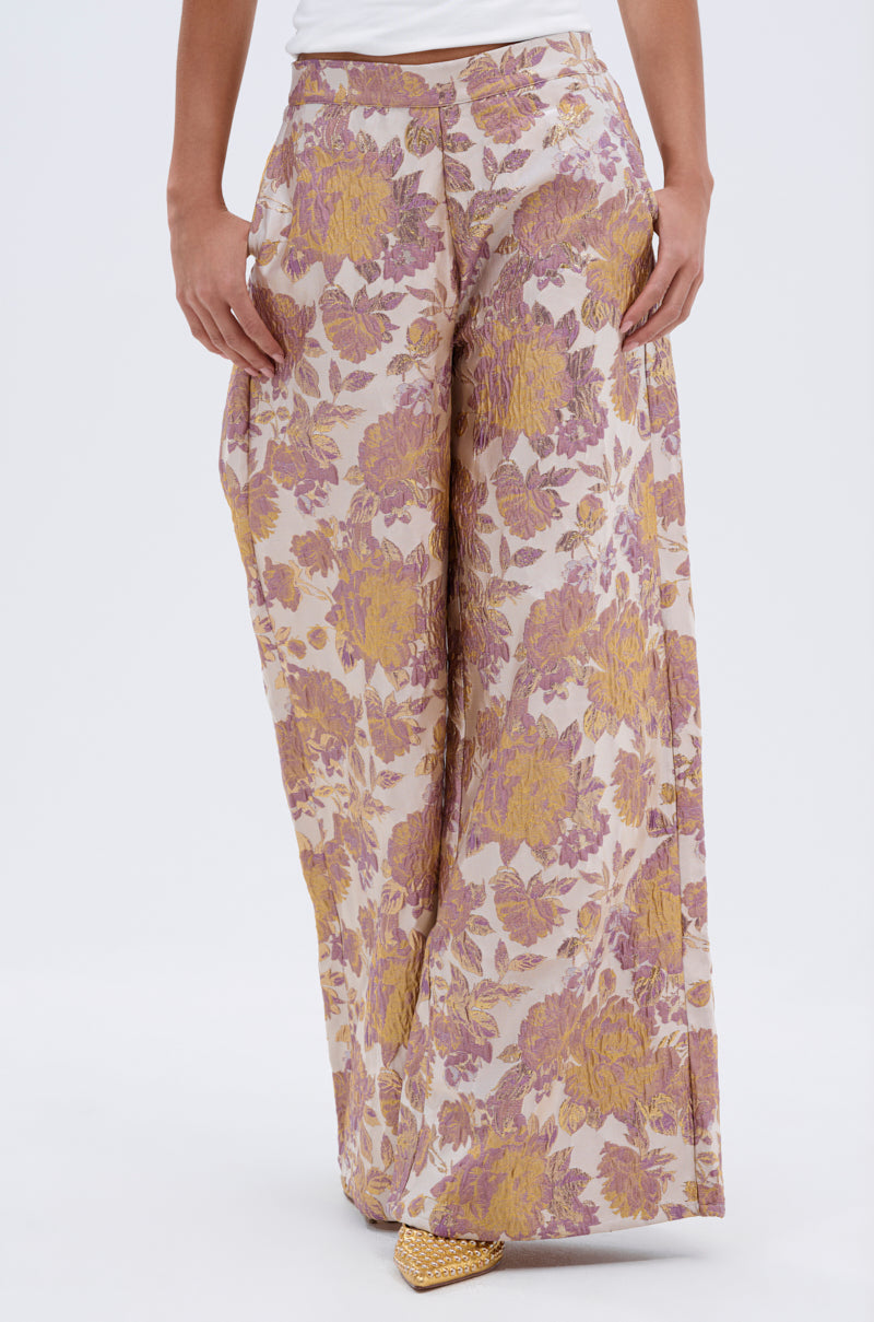 Wearing the SLOW MOTION BROCADE TROUSER—high-rise with a pink, gold, and purple floral design—styled with a white top and yellow pointed-toe shoes. 2