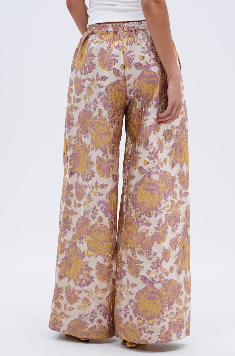 Wearing the SLOW MOTION BROCADE TROUSER—wide-leg, high-rise pants with gold, pink, and purple floral brocade—a person stands against a plain white background. 4