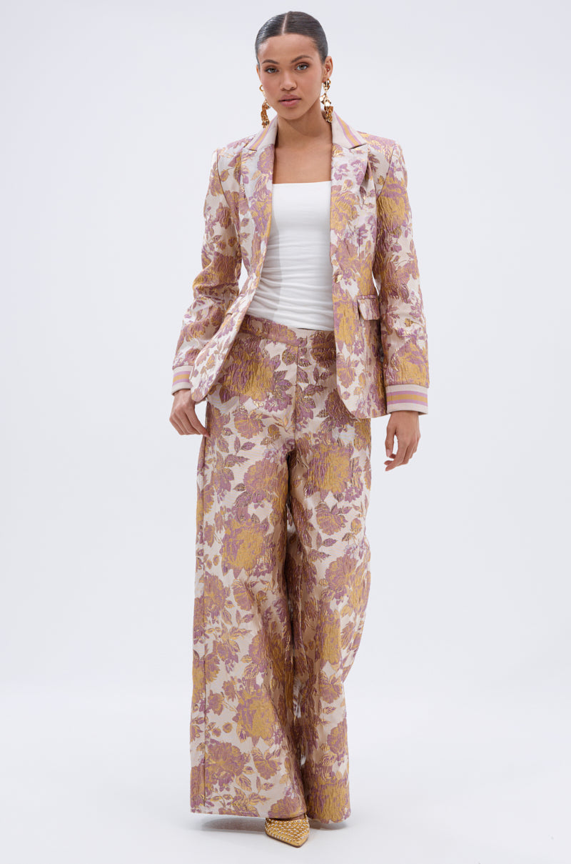 A woman poses against a white background wearing SLOW MOTION BROCADE TROUSER, a gold and pink floral-patterned, high-rise, wide-leg style, paired with a matching blazer, white tube top, gold earrings, and pointed shoes. 7