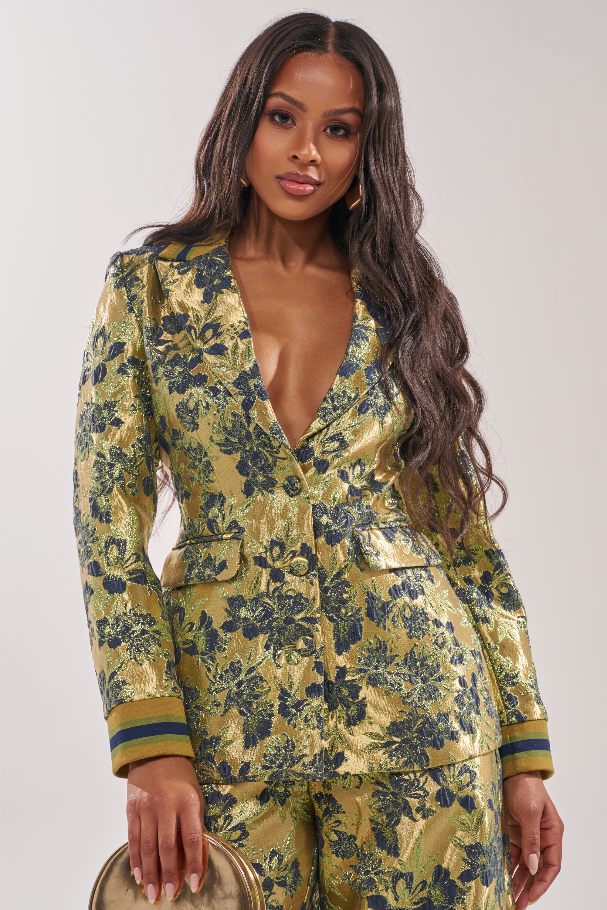 A woman with long, wavy hair wears the HARLOW BROCADE BLAZER and matching pants with embroidered floral details. She carries a small round gold purse and stands against a plain light background. 2