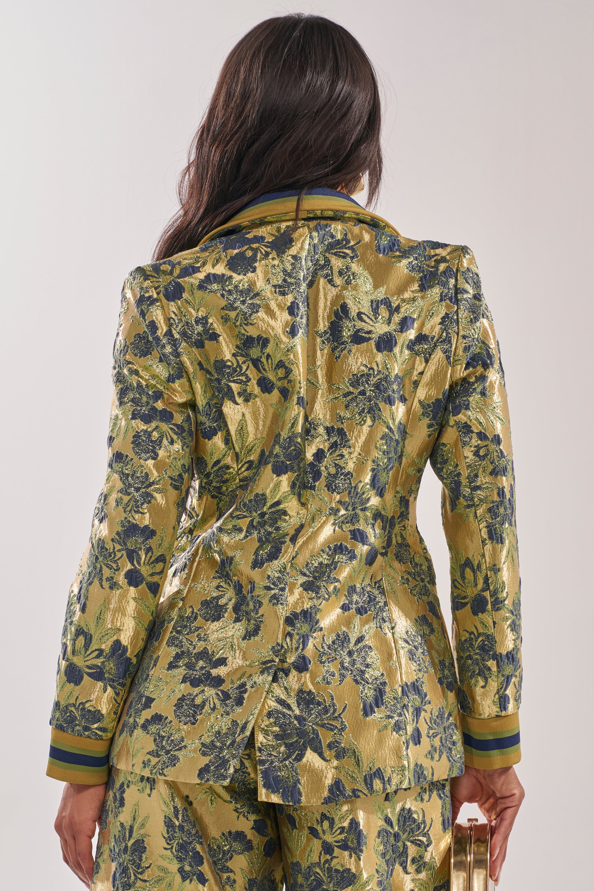 A person with long brown hair is shown from the back wearing the HARLOW BROCADE BLAZER, featuring a metallic blue and green floral pattern, tailored silhouette, colored cuff trim, embroidered details, and a central back vent. 4