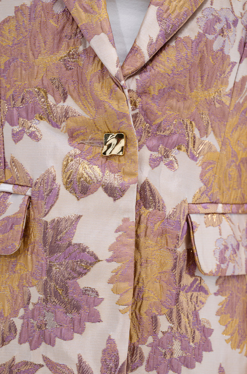 Close-up of the SLOW MOTION BROCADE BLAZER, featuring a floral pattern in gold, lavender, and pink with two flap pockets, a gold square button, and textured metallic brocade fabric.