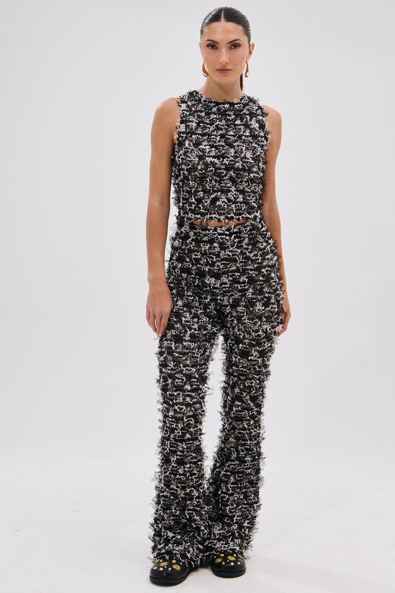 A woman stands against a plain background wearing the CRAZY FOR YOU FRINGE TANK, a sleeveless black and white textured crop top, paired with high-waisted flared pants and black shoes. Her hair is styled back and her expression is neutral. 5