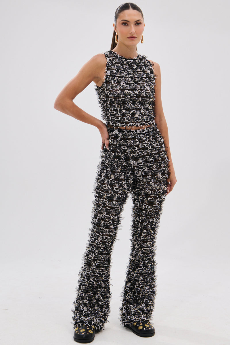 A woman stands against a white background wearing the CRAZY FOR YOU FRINGE TANK, a black and white fuzzy-patterned cropped sleeveless top paired with matching high-waisted flared pants. She has straight hair pulled back and wears black shoes. 6