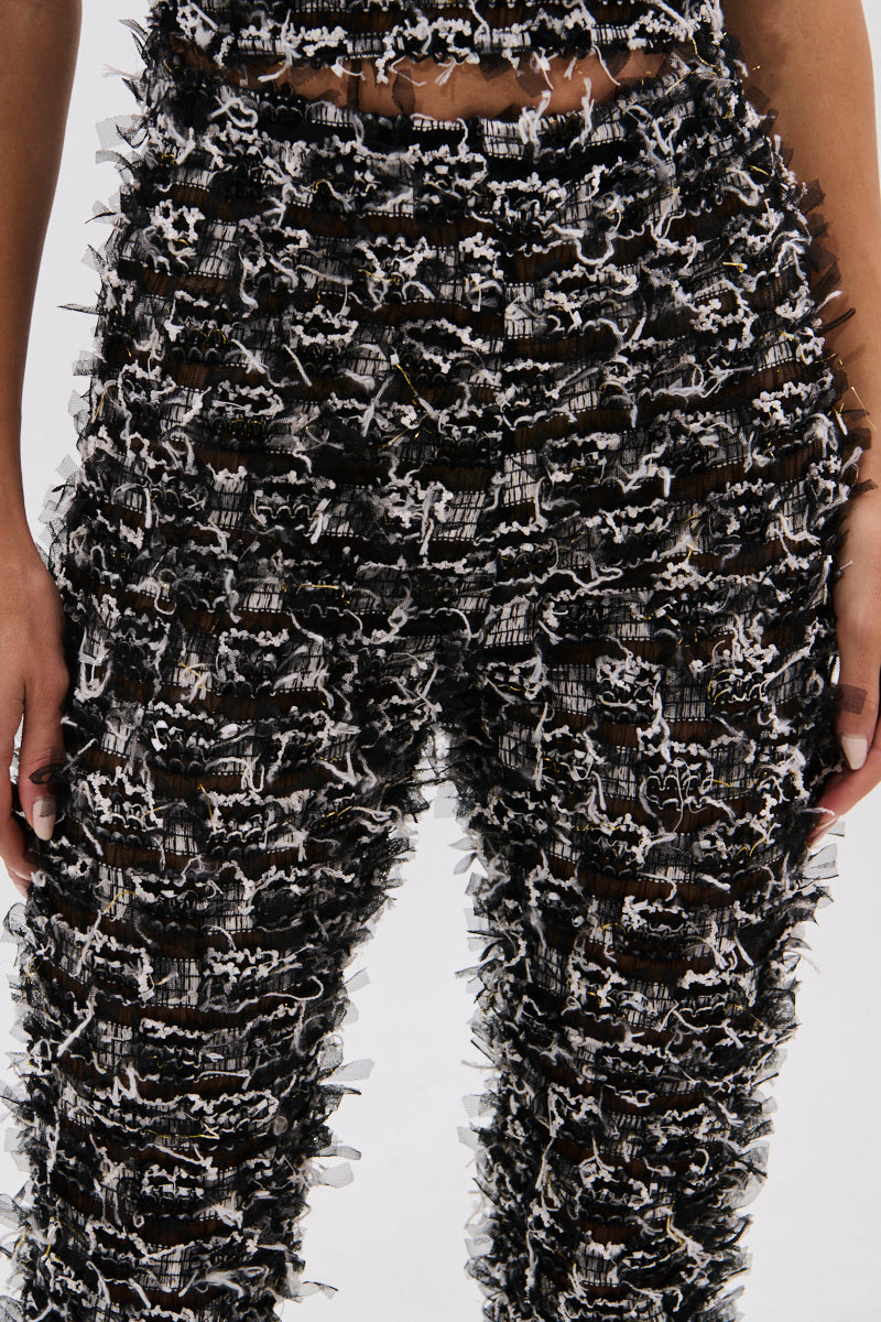 Close-up of a person wearing CRAZY FOR YOU FRINGE FLARE LEGGING—high-rise, black-and-white pants with layered, frayed fringe details. Only the torso and upper legs are shown; perfect for music festivals against a plain background. 7
