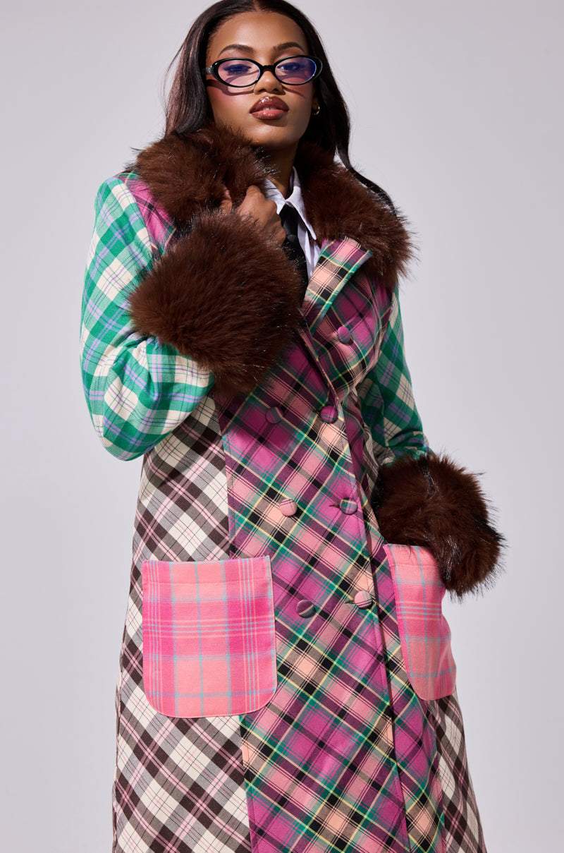 A woman wears the SWEET THING PATCHWORK TRENCH featuring a colorful patchwork design, large pink pockets, and brown faux fur trim on the collar and cuffs. She pairs it with purple glasses and stands confidently against a plain background.