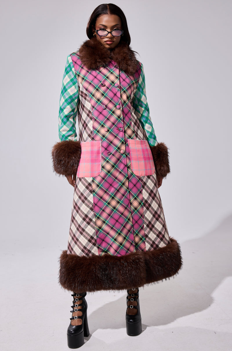 A glasses-wearing model showcases the SWEET THING PATCHWORK TRENCH, a long faux fur trim coat with green, pink, and brown patterns, large pink plaid pockets, and patchwork styling—styled perfectly with platform boots.