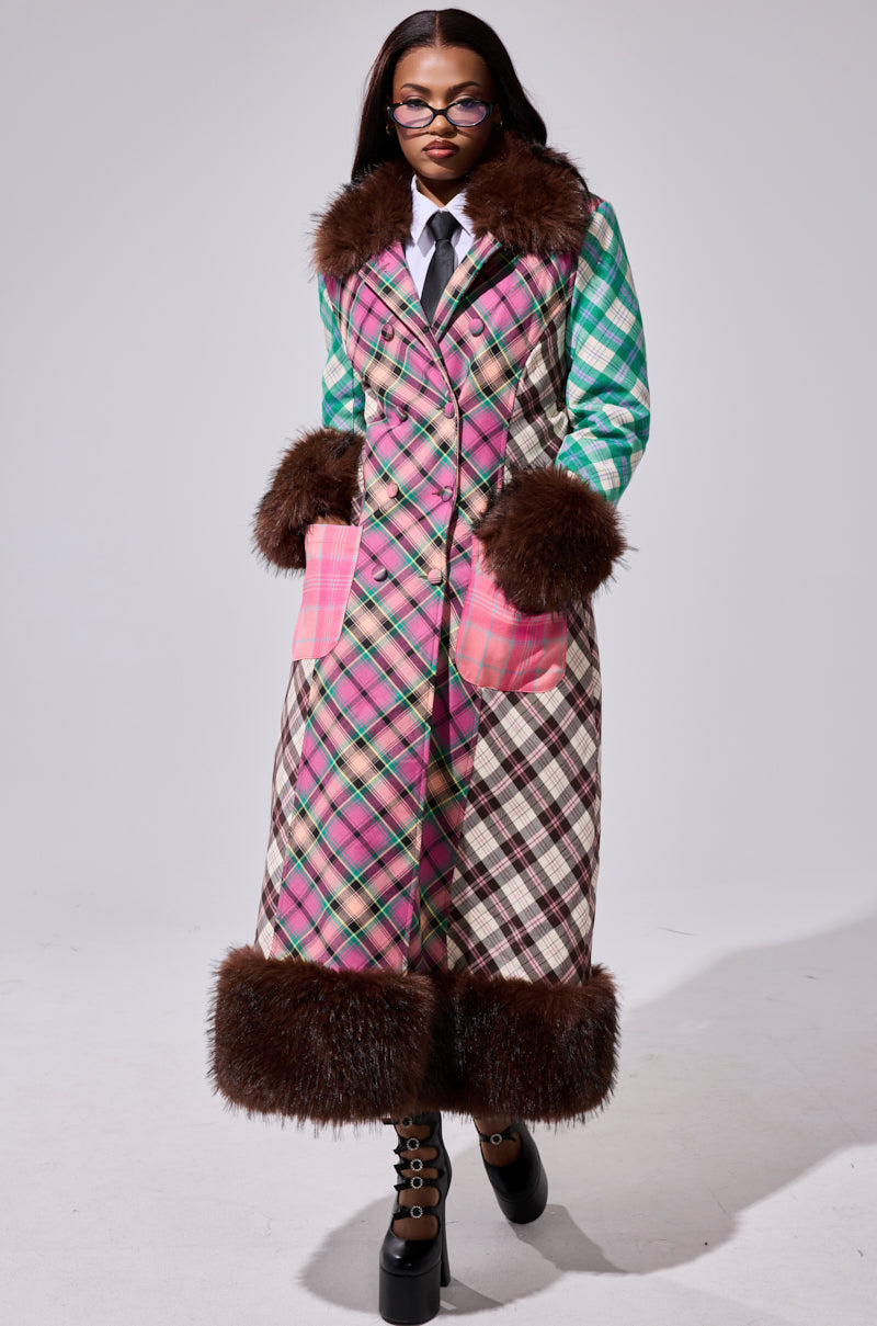 A woman in the SWEET THING PATCHWORK TRENCH with brown faux fur trim, styled over a white shirt and tie, black platform shoes, and glasses, stands against a plain light background.