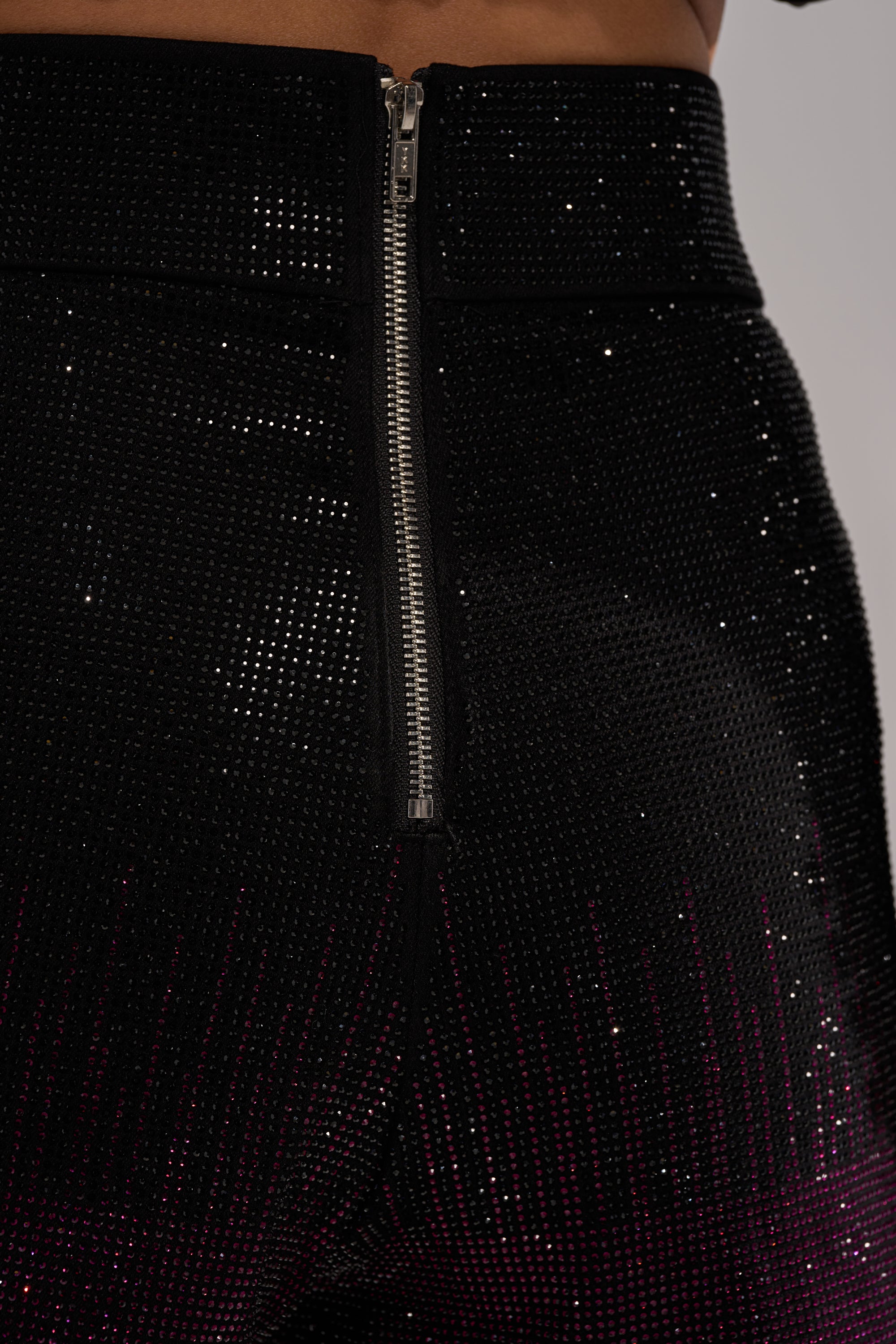 Close-up of a person wearing the RAISE A GLASS RHINESTONE SHORTS—high-waisted black shorts adorned with sparkling rhinestones and a visible metallic zipper at the back.
