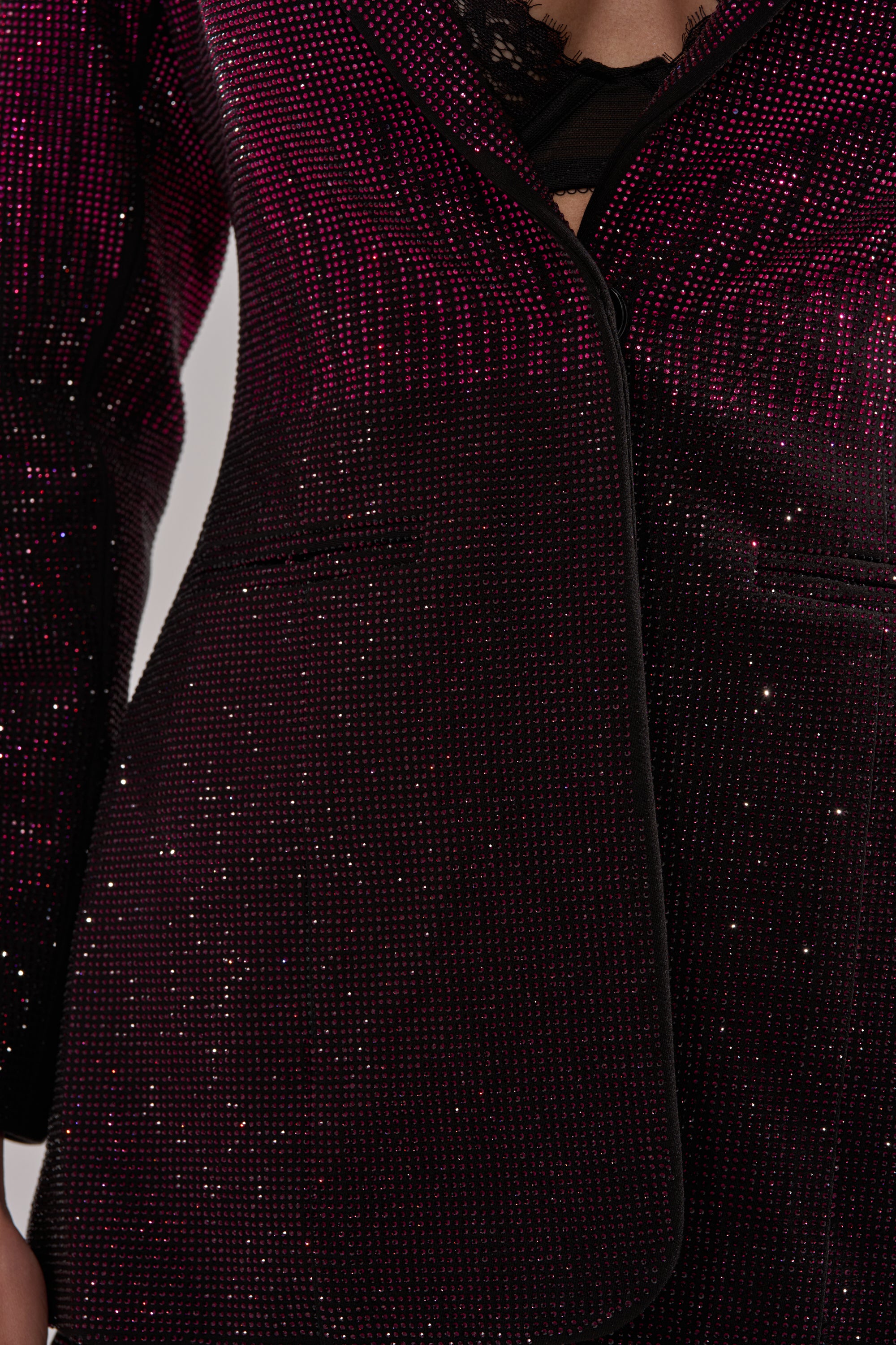 A close-up of a person wearing the RAISE A GLASS RHINESTONE BLAZER—a dark purple blazer with sparkling rhinestone details—paired with a glimpse of a black lace top underneath.