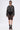 A person poses against a plain background wearing the SPOTLIGHT RHINESTONE BOMBER, a sheer black lace skirt layered over black undergarments, black mesh socks with open-toe heels, layered necklaces, and oversized sunglasses.