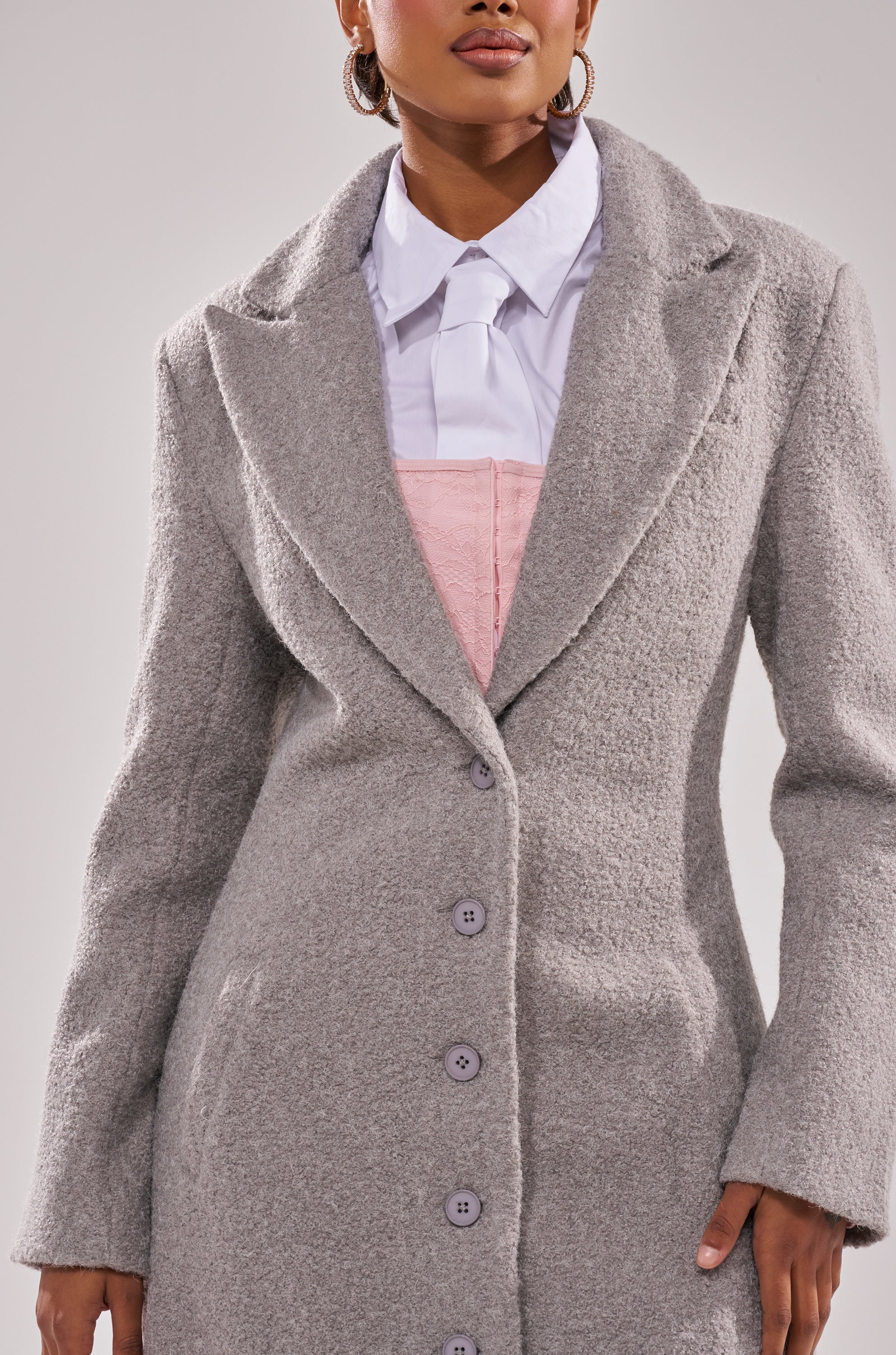Wearing the MAKE IT LAST BOUCLE TRENCH over a white collared shirt and light pink bustier, the person’s face is partially out of frame against a plain, light background.