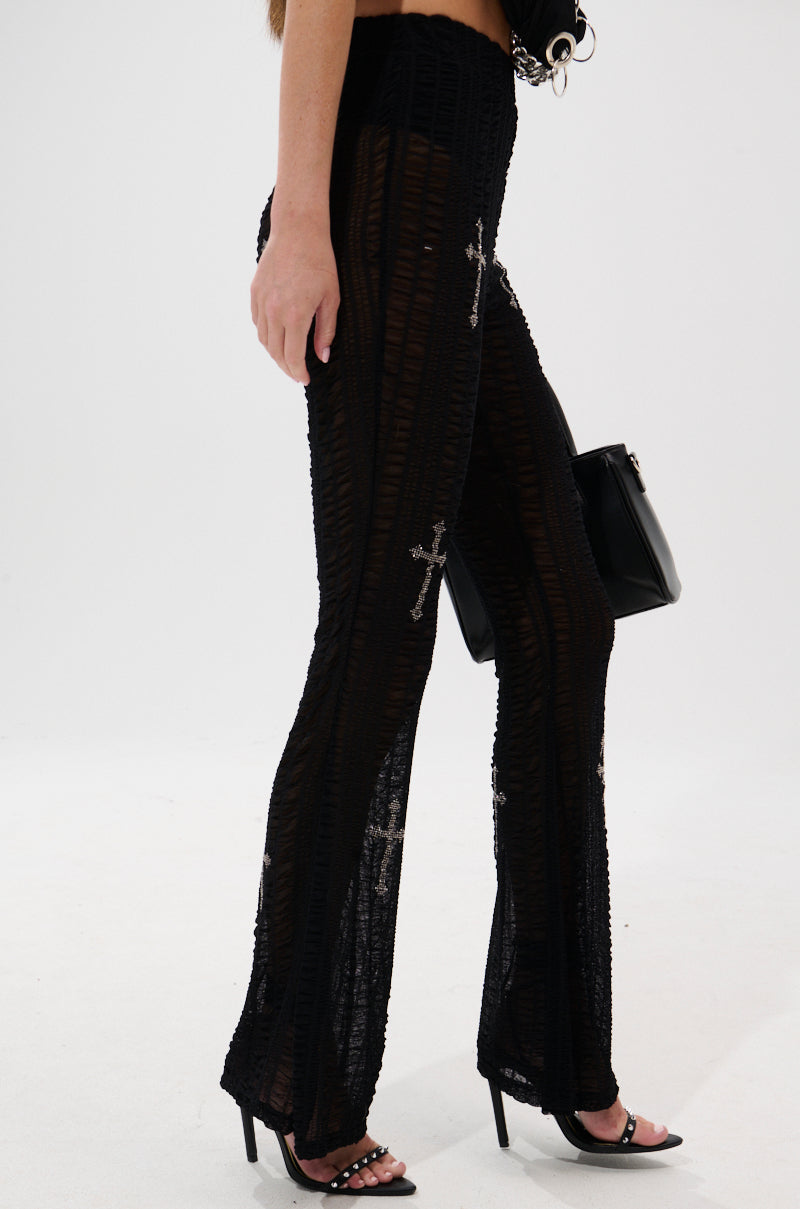 A person in BLESSED MESH LEGGING pants with rhinestones and flared legs, black high-heeled sandals, and a black handbag walks against a plain white background. 2